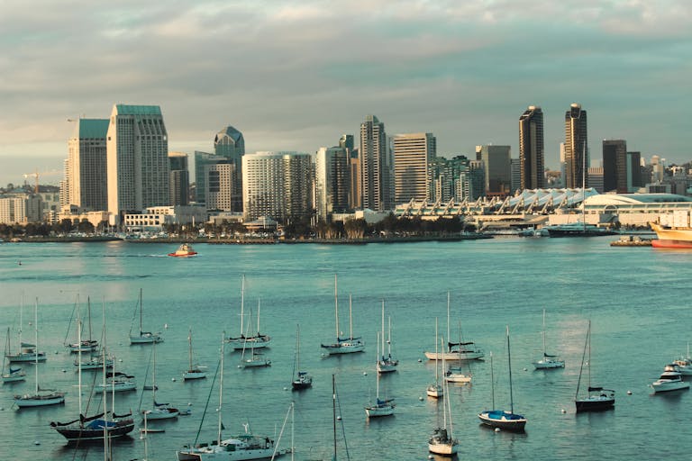 A picturesque view of the San Diego skyline with sailboats anchored in the harbor under a cloudy sky.