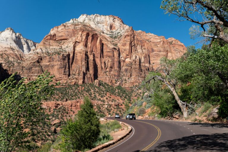 Captivating view of Zion National Park's towering red cliffs along a winding road under a clear blue sky.