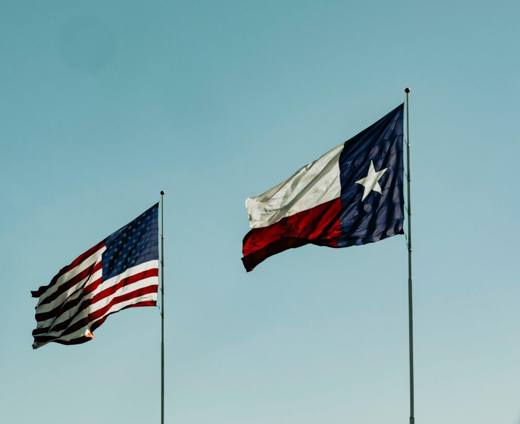 American and Texas flags waving under a clear blue sky, symbolizing patriotism and freedom.