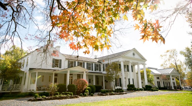 Beautiful colonial-style house with a scenic autumn backdrop and vibrant foliage.