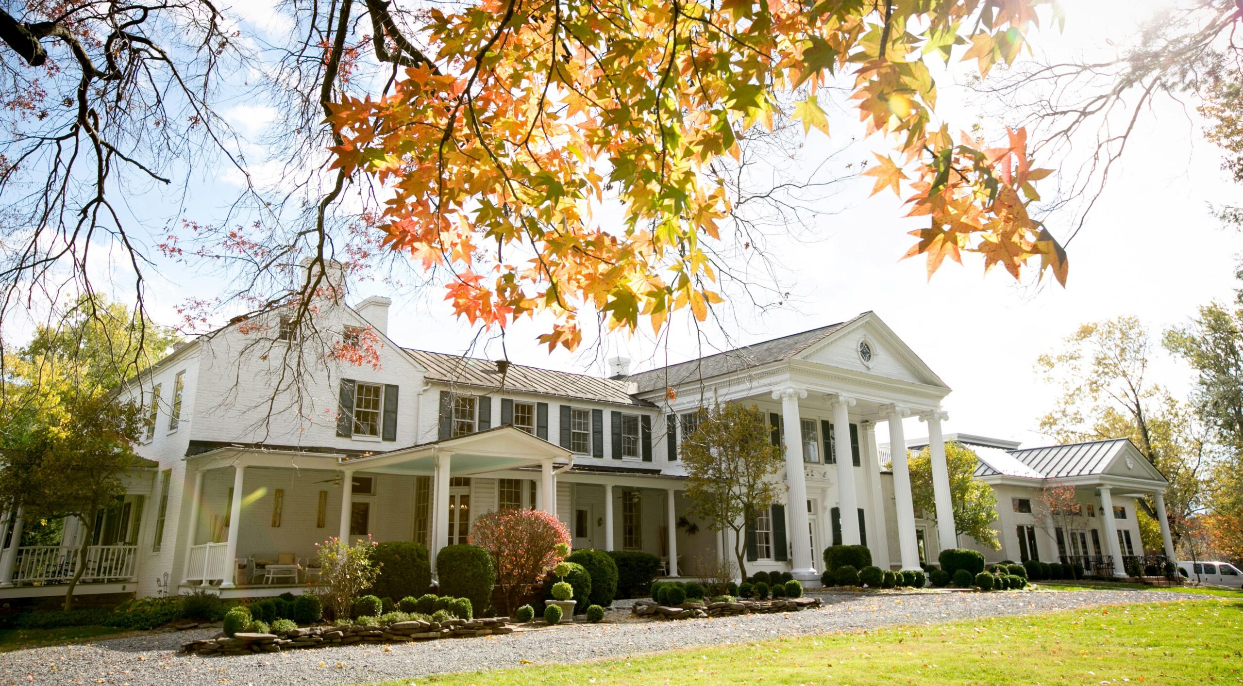 Beautiful colonial-style house with a scenic autumn backdrop and vibrant foliage.