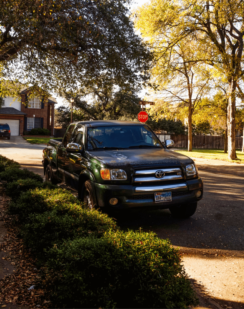 A black pickup truck parked on a quiet suburban street lined with trees and houses.